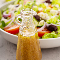 Glass bottle of salad dressing with a salad in the background