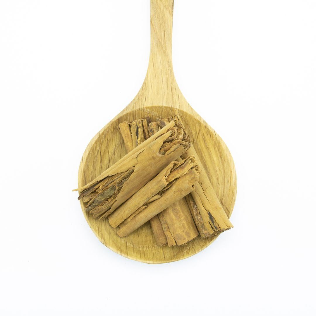A wooden spoon holding several sticks of cinnamon, placed against a white background.