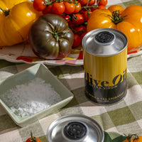 Extra Virgin Olive Oil next to a bowl of white flake sea salt and tomatoes