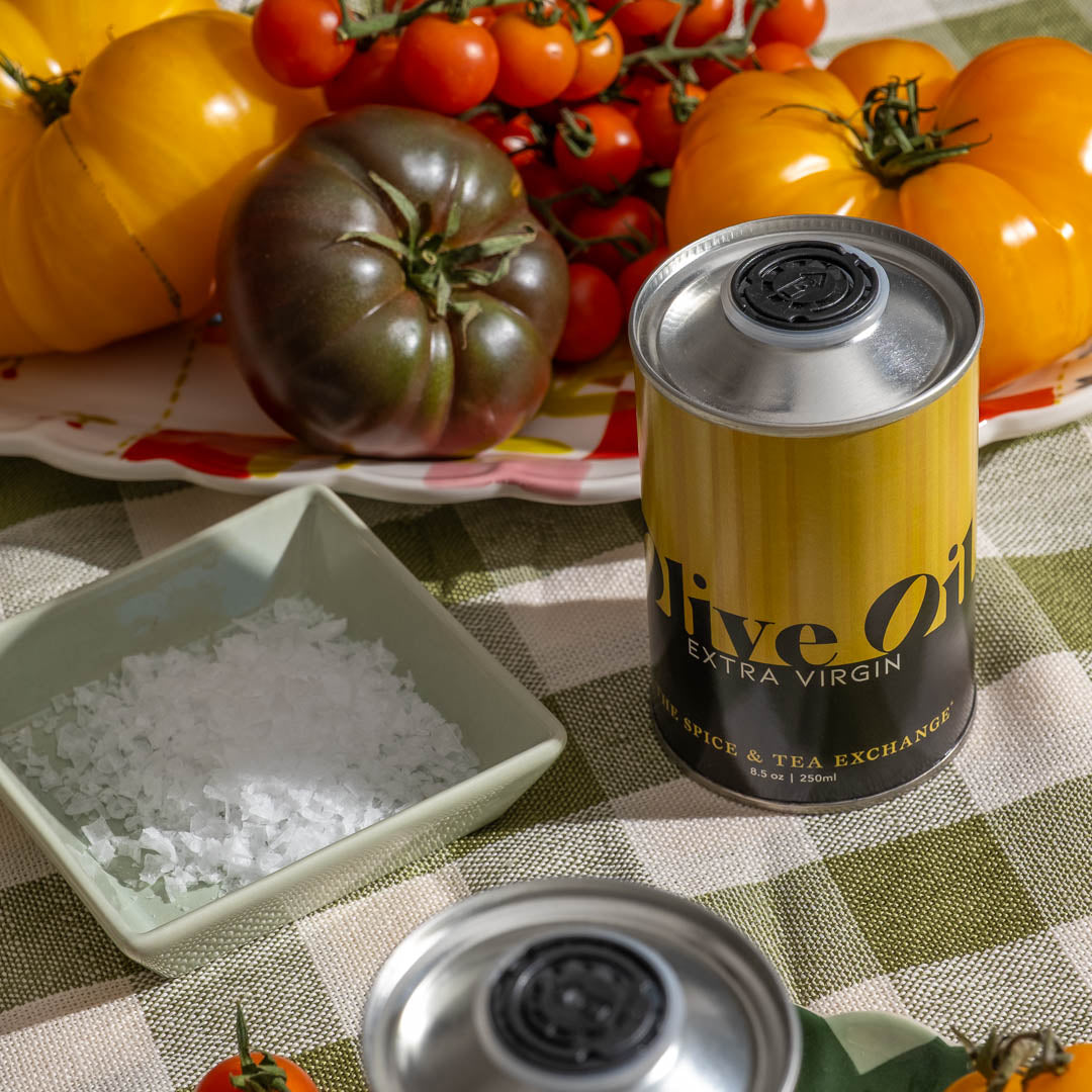 Extra Virgin Olive Oil next to a bowl of white flake sea salt and tomatoes