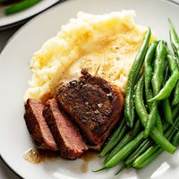 Plated dish with sliced beef, mashed potatoes, and green beans on a white plate.
