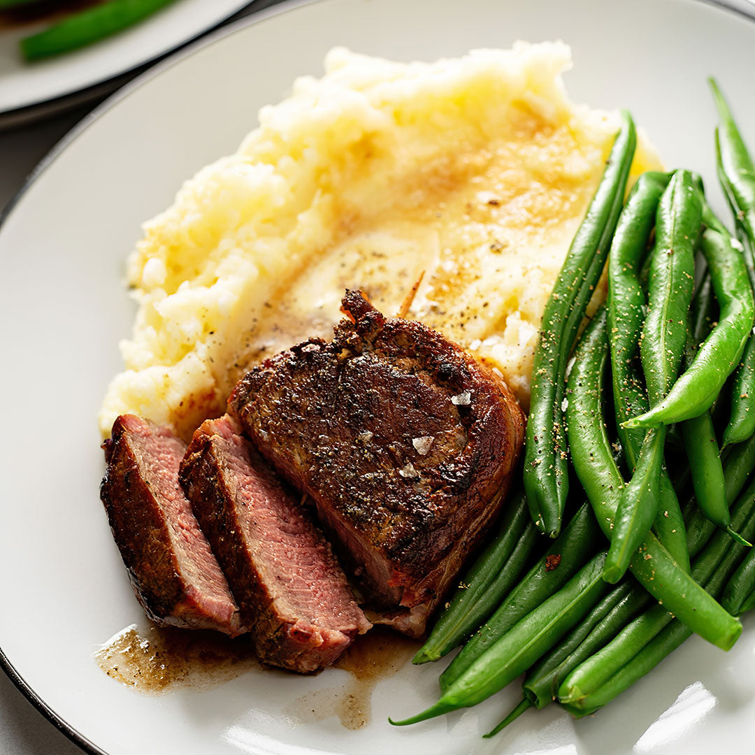 Plated dish with sliced beef, mashed potatoes, and green beans on a white plate.
