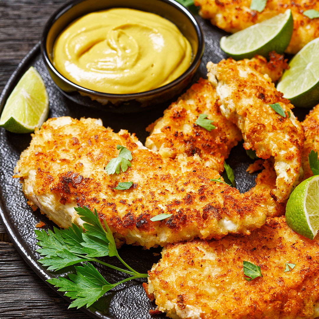 Breaded and fried chicken pieces on a plate with mustard and lime wedges.