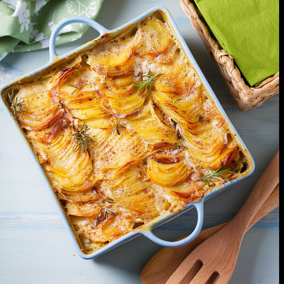 Baked dish with layered potatoes in a blue baking dish on a light blue surface.