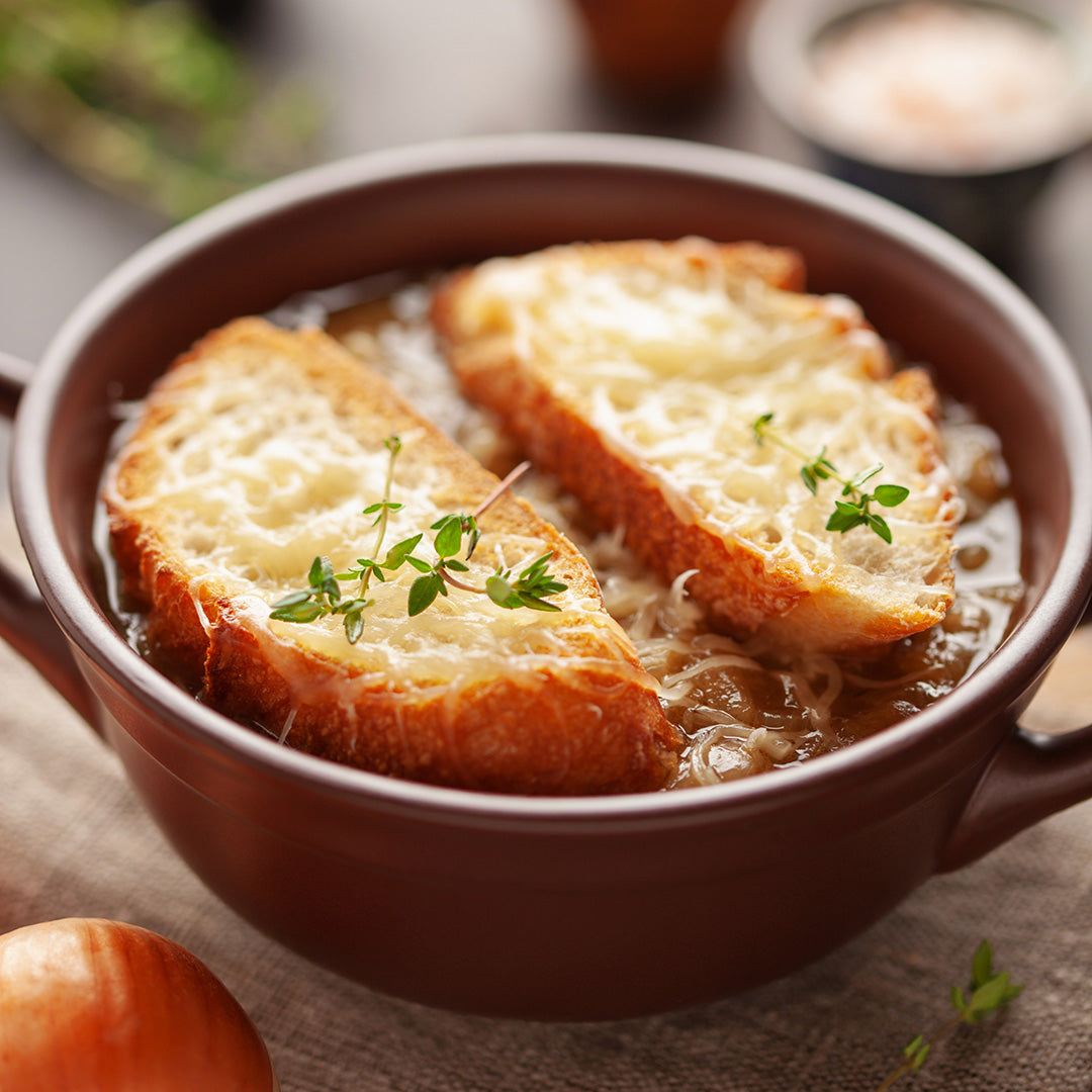 Bowl of French onion soup with toasted bread slices and thyme leaves on a wooden table.