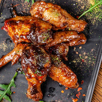 Glistening chicken wings on a dark surface with garnishes