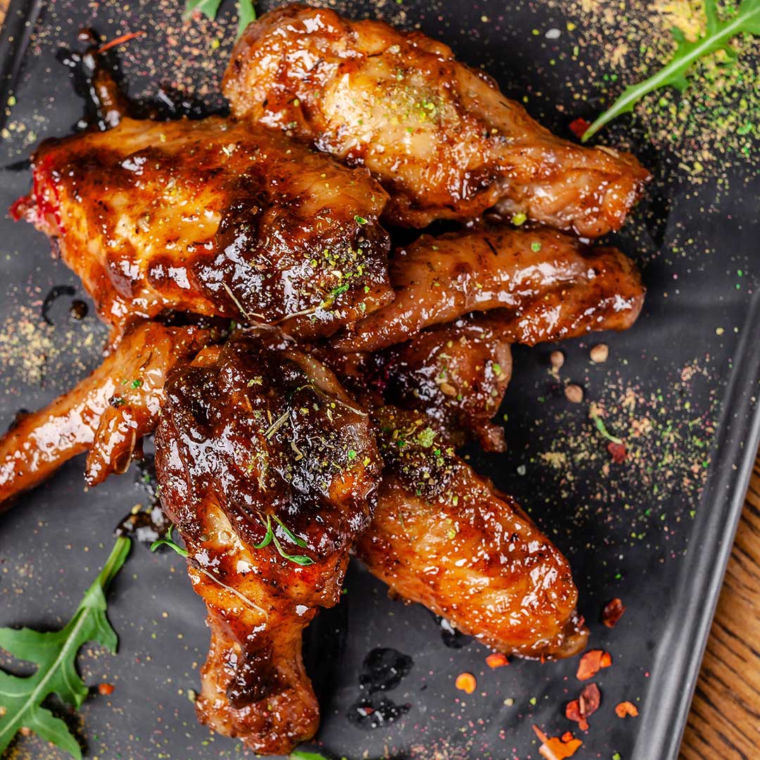 Glistening chicken wings on a dark surface with garnishes