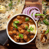 Tandoori chickpea curry in a bowl with naan bread, onions, and green chilies